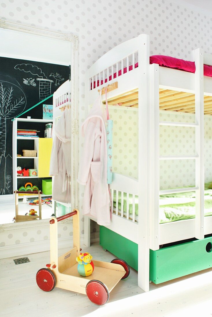 White bunk beds and push-along cart in front of full-length mirror in children's bedroom