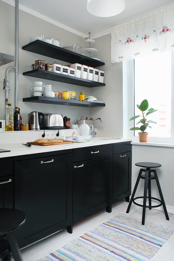 Küche mit schwarzen Unterschränken und weisser Arbeitsplatte, oberhalb schwarze Ablagen an grauer Wand