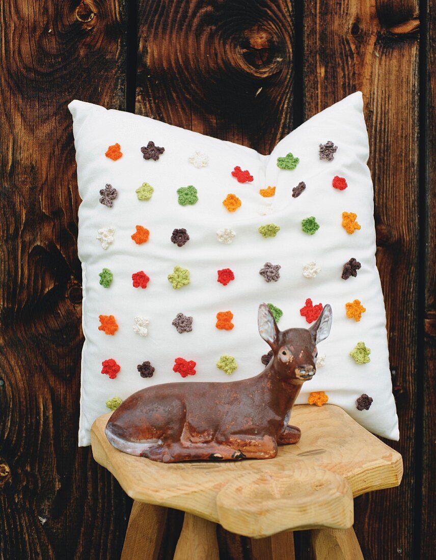 Retro deer figurine on wooden stool in front of cushion with appliqué crocheted flowers