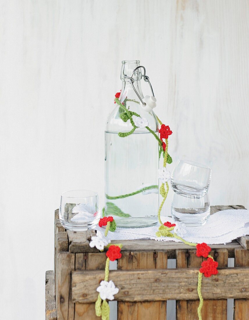 Garland of crocheted flowers draped around vintage glass bottle on rustic wooden crate