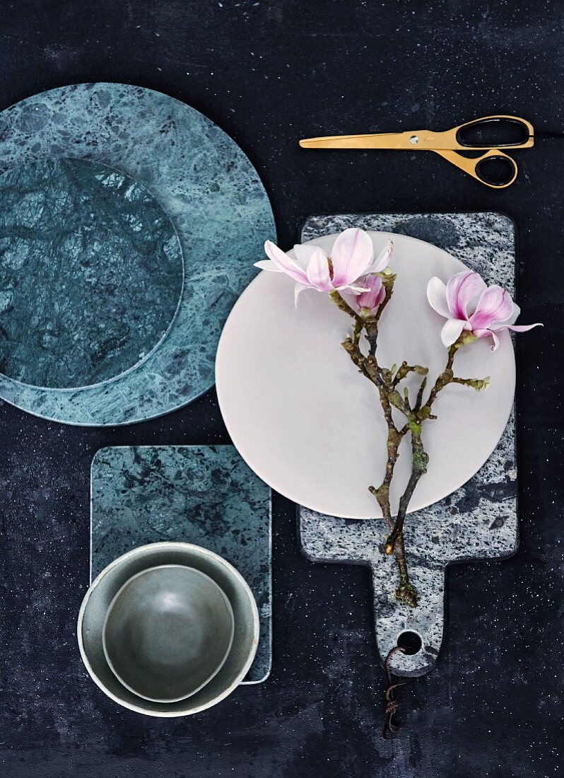 Green marble boards, ceramic dish and branches of flowering magnolia on marble board with leather strap