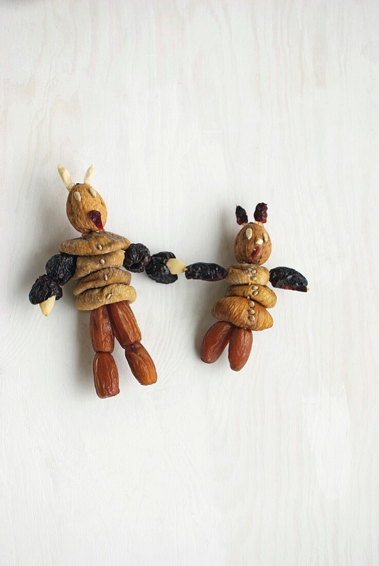 Figurines made from dried dates and figs on white surface