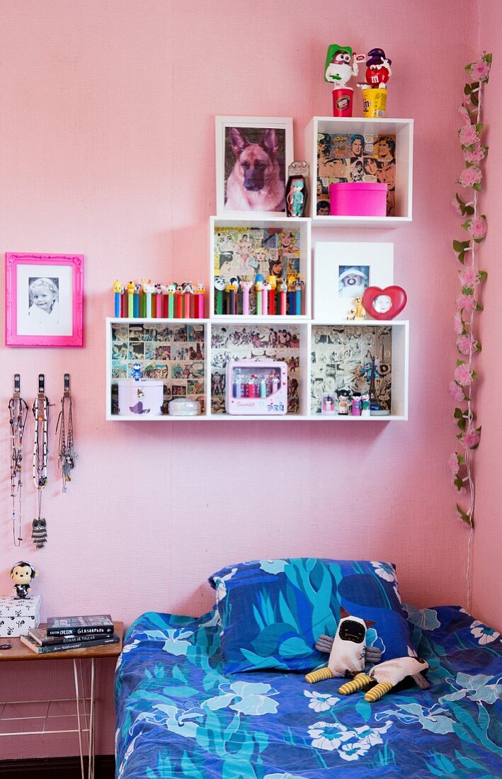 Blue bed linen on single bed and white modular shelving in child's bedroom with pink walls