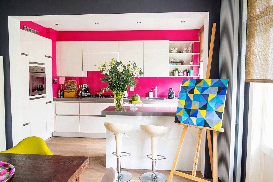 Blick in offene Küche mit modernen weißen Möbeln und pinker Wand