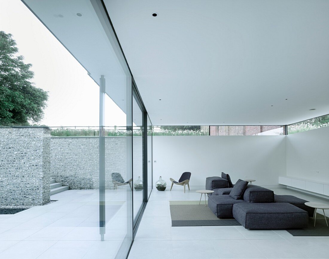 Loungebereich in weißer Luxuswohnung mit minimalistischer Designer-Möblierung, Glasfront, Terrasse und Natursteinmauer
