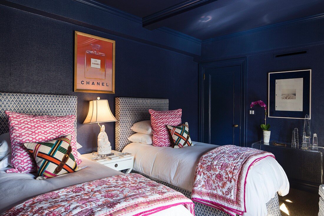 Dunkelblaues Schlafzimmer mit zwei Einzelbetten, gepolstertem Betthaupt und gemusterten Kissenbezügen, eklektisches Flair