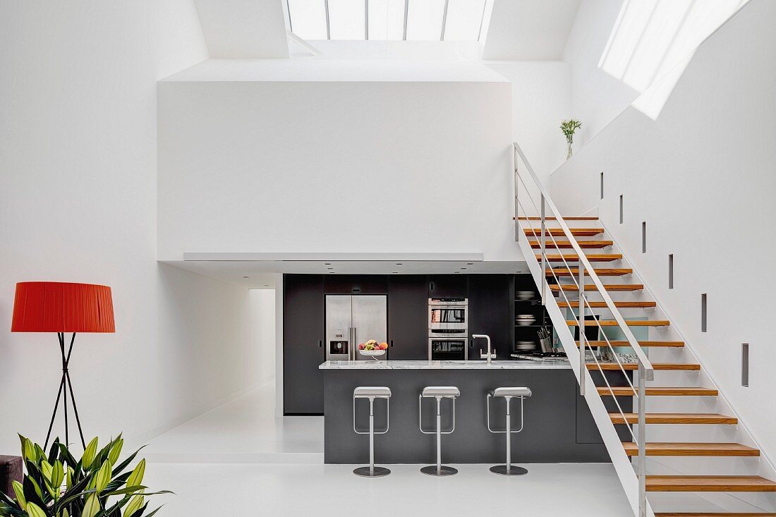 Stahltreppe mit Holzstufen zur weißen Galerieebene über anthrazitfarbener Designerküche