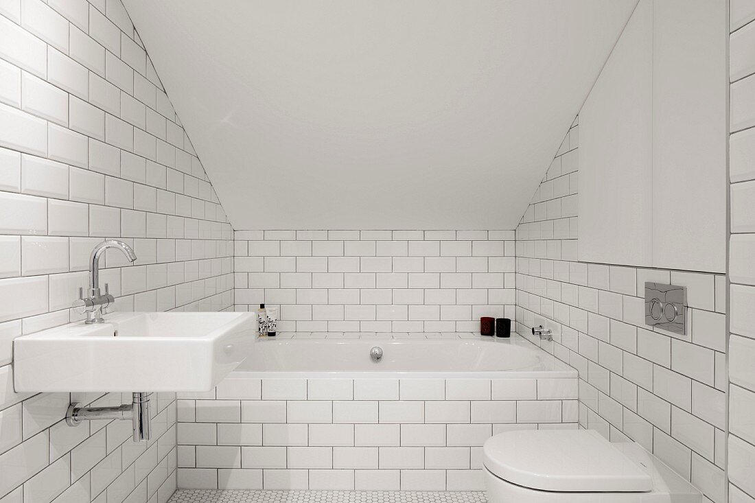 Weiß gefliestes Bad mit Badewanne und Toilette im Dachgeschoss