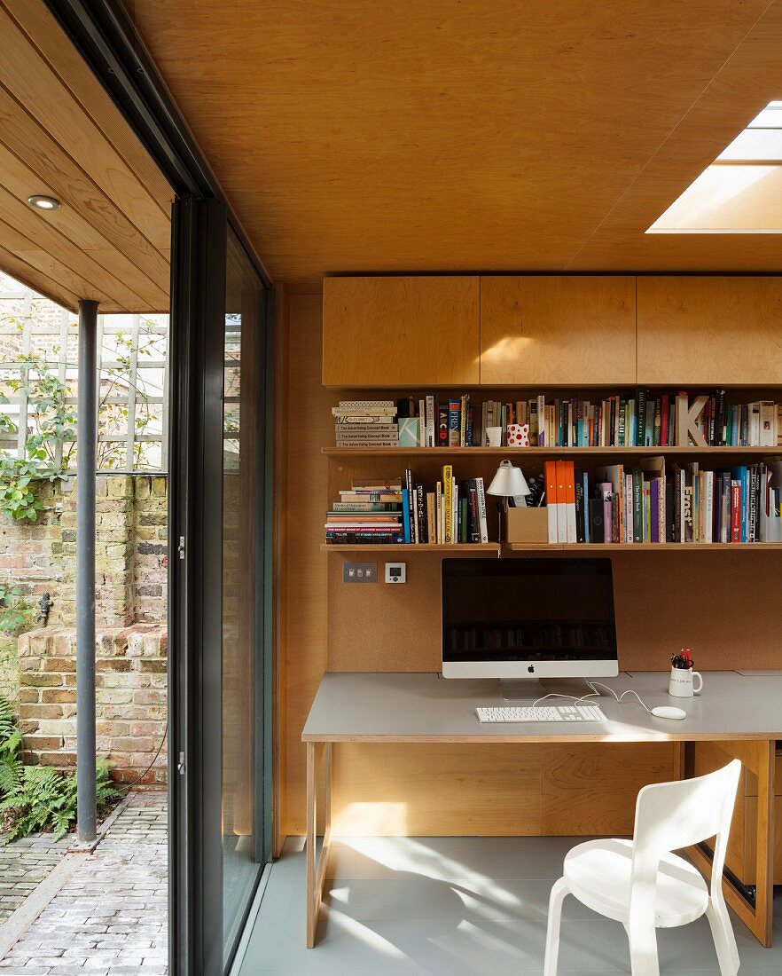 Computer on desk in modern extension with wood cladding, skylight and open terrace doors