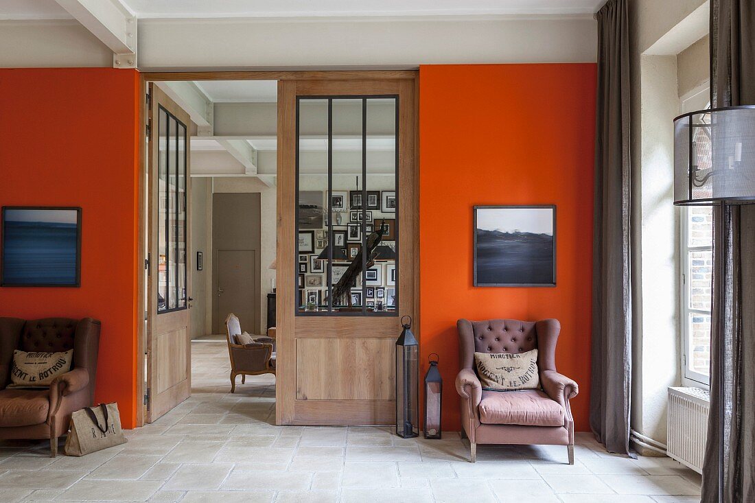 Two armchair below artworks on orange wall flanking door