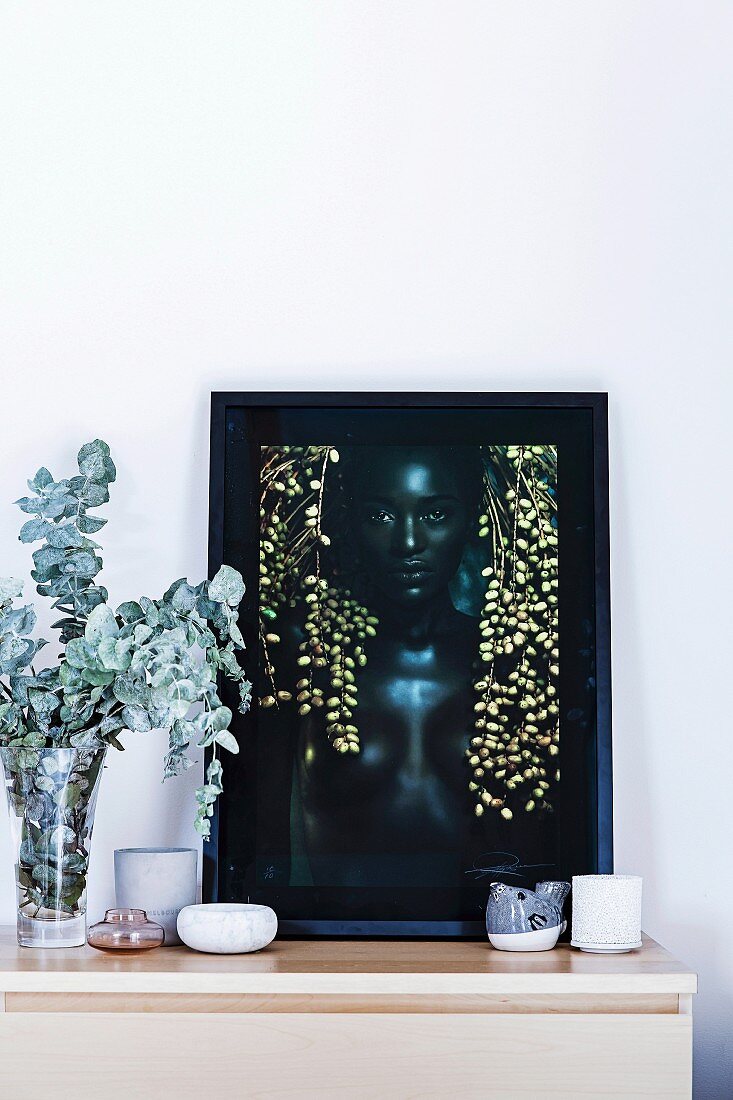 Framed portrait photo and decorative bowls on a sideboard with a leaf branch in a glass vase