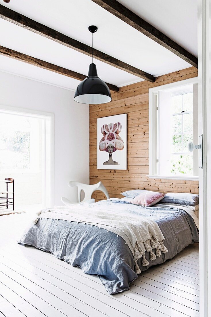 Doppelbett mit Überwurf vor Holzwand in Schlafzimmer mit Holzbalkendecke