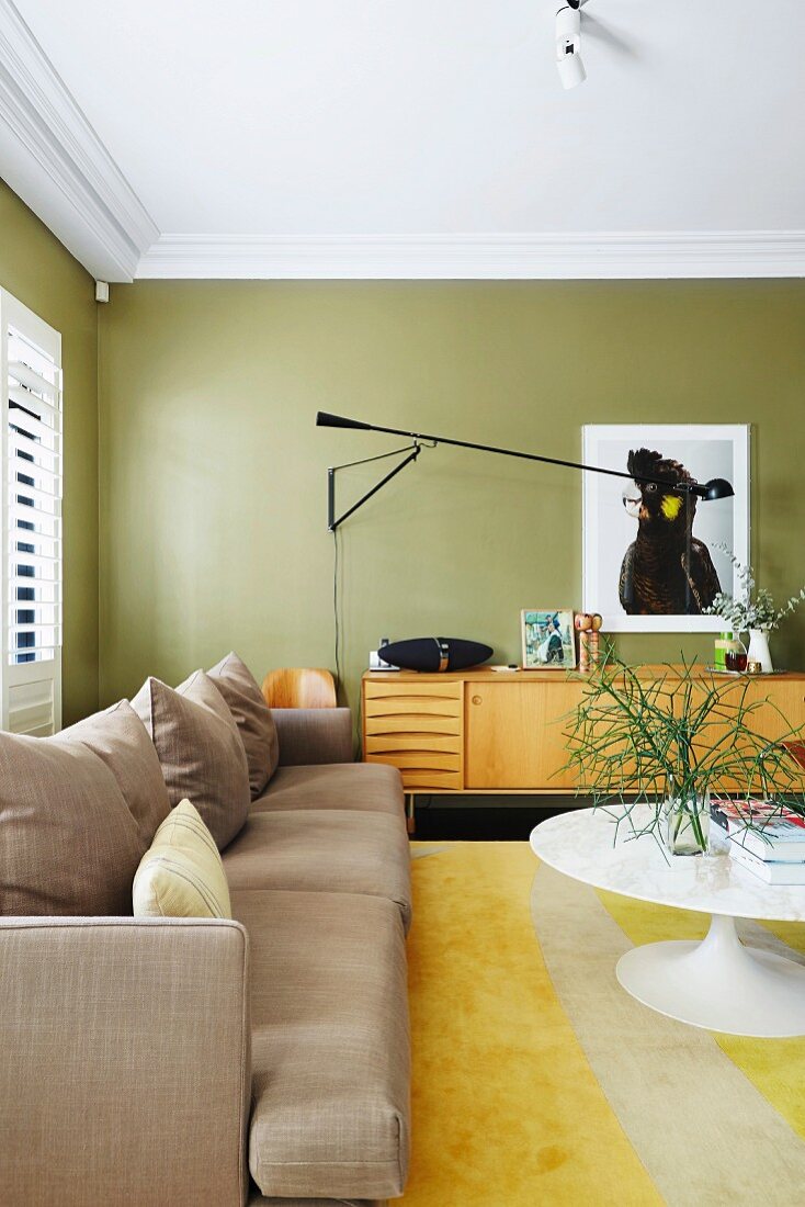 Light upholstered sofa and tulip table in olive green living room with retro flair