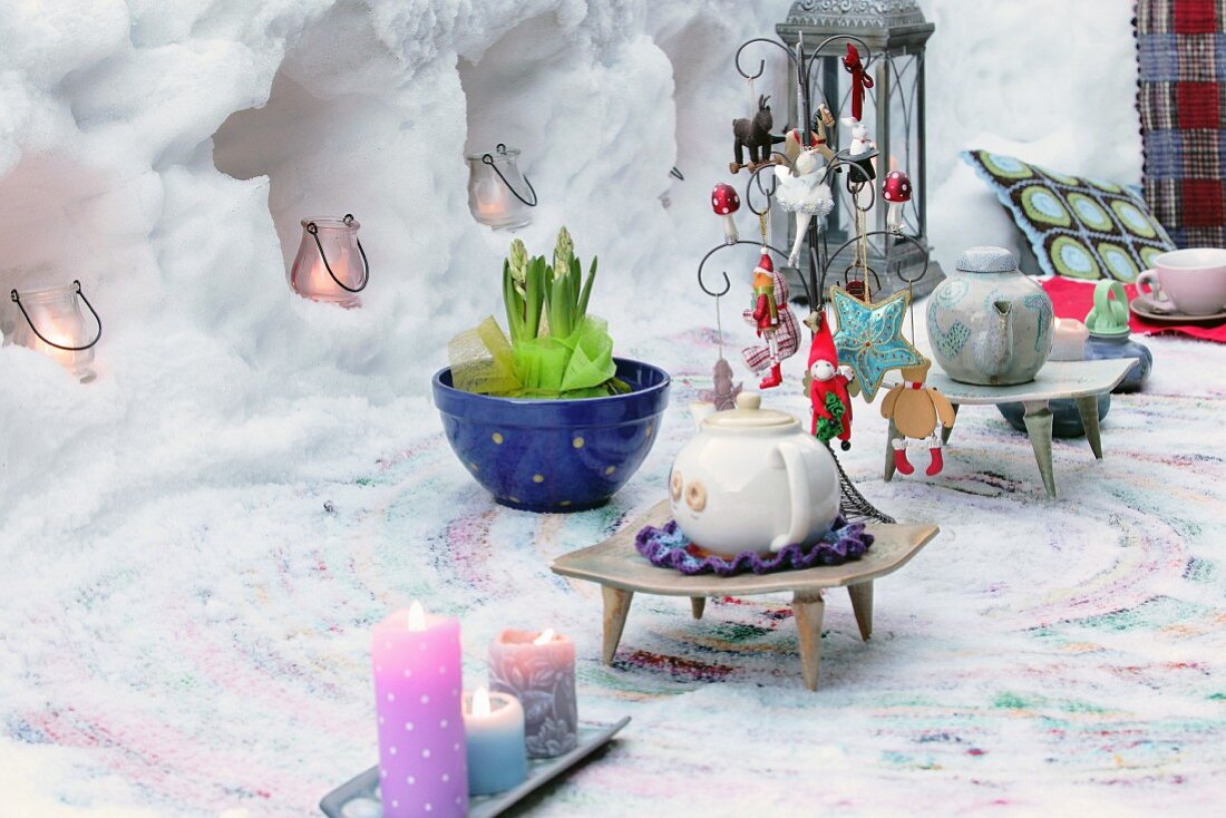 Teekannen auf geschmücktem Tisch vor ausgehöhlter Schneemauer mit Windlichtern