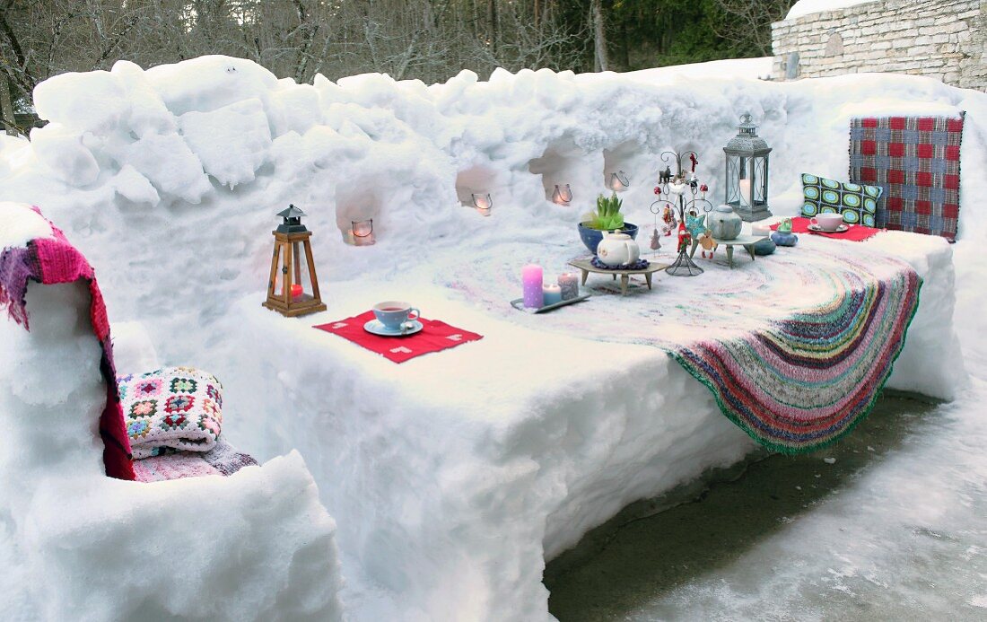 Mit Kerzen und Laternen dekoriertem Schnee-Tisch auf verschneiter Terrasse