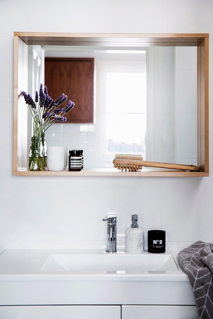 White washstand, above wall mirror with wooden frame as a shelf with bathroom accessories