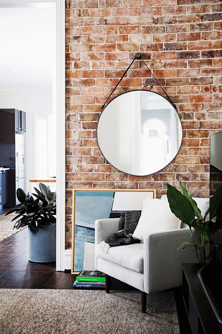Round wall mirror on brick wall, including a white armchair in a renovated old building