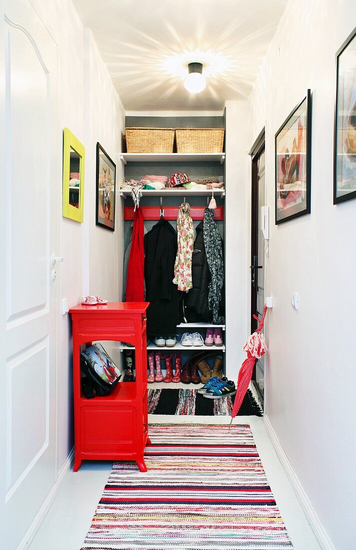 In Wandnische eingebaute Garderobe mit Regalbrettern und Garderobenhakenleiste, davor Flickenteppiche und rotes Ablageschränkchen
