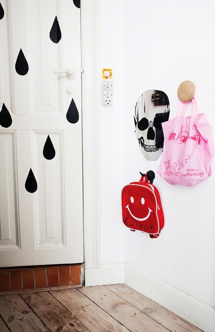 Garderobe mit Kindertaschen an Wandhaken neben Totenkopf und Haustür mit schwarzen Tropfenmotiven