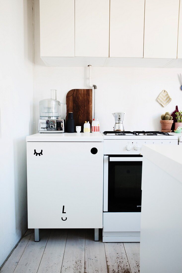 weiße Küchenzeile mit Hängeschränken, Türfront mit sitlisiertem 'Gesichtsmotiv' dekoriert
