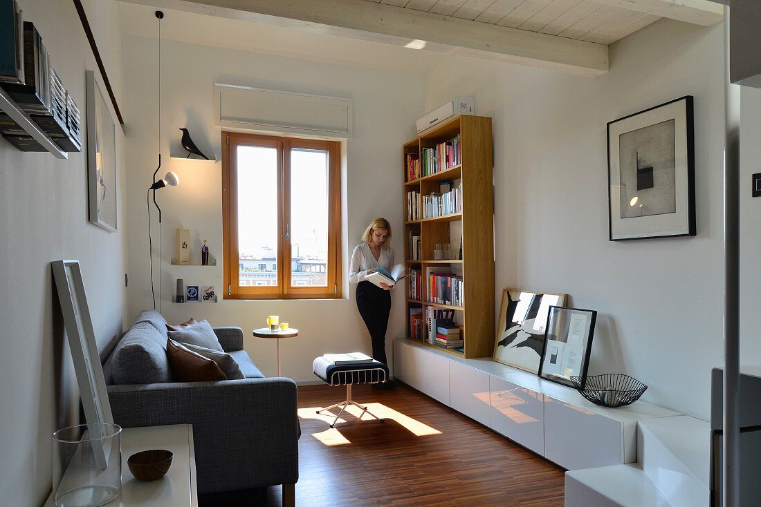 Renoviertes Wohnzimmer mit lesender Frau zwischen Bücherregal und Fenster