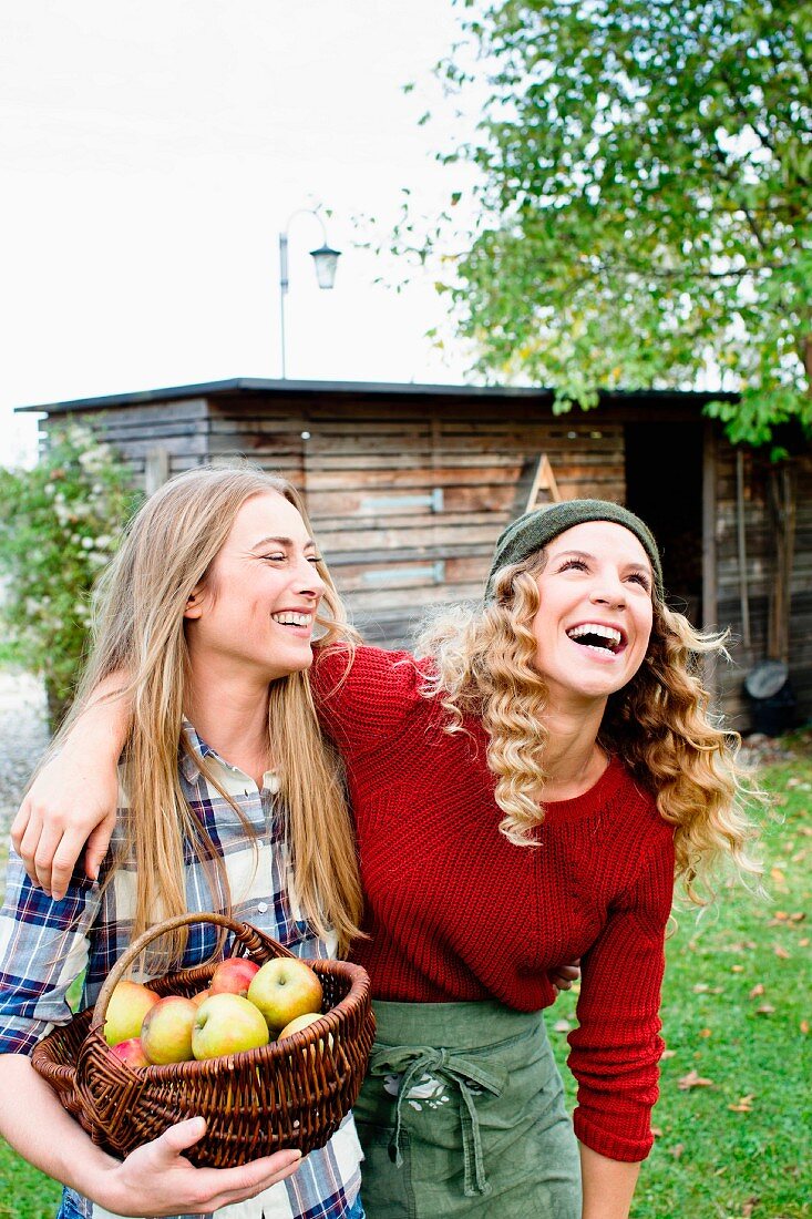 Lachende Frauen im Garten mit einem Korb frisch geernteter Äpfel