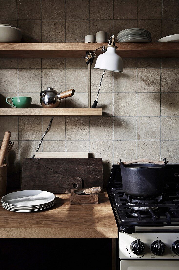 Küchenzeile mit Holzarbeitsplatte und Wandregalbrettern vor Fliesenwand, daneben Gasherd