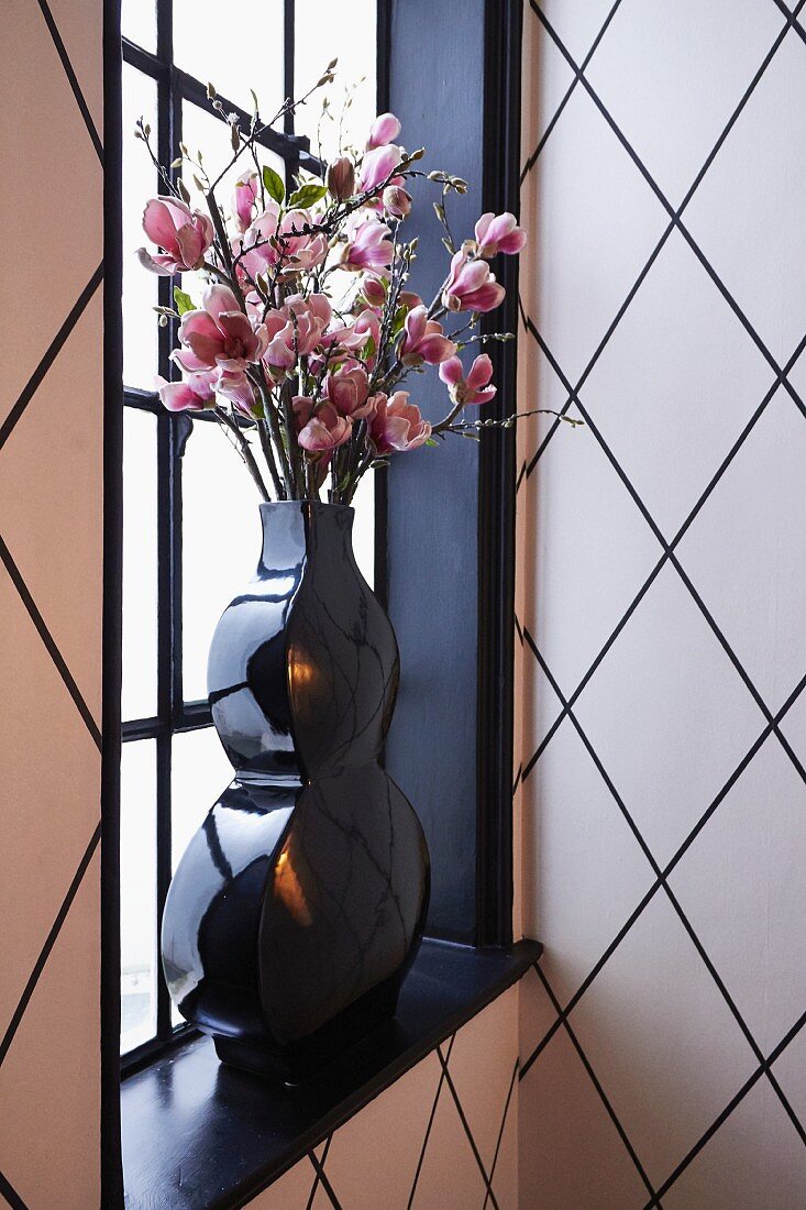 Branches of pink flowers in black vase in front of lattice window