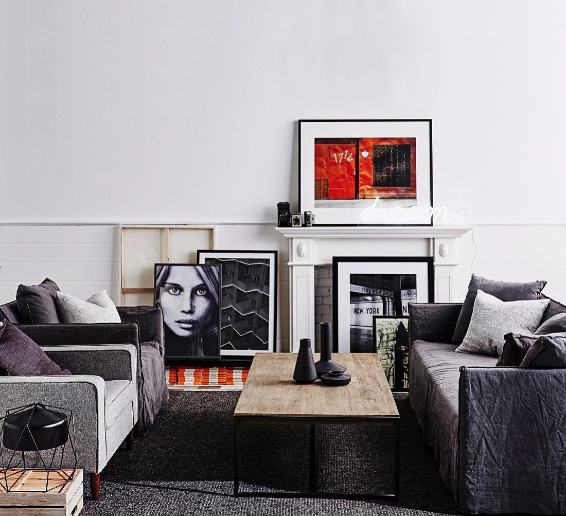 Sofagarnitur in Grautönen und Couchtisch mit rustikaler Tischplatte, weiße Kaminverkleidung und gerahmte Fotokunst
