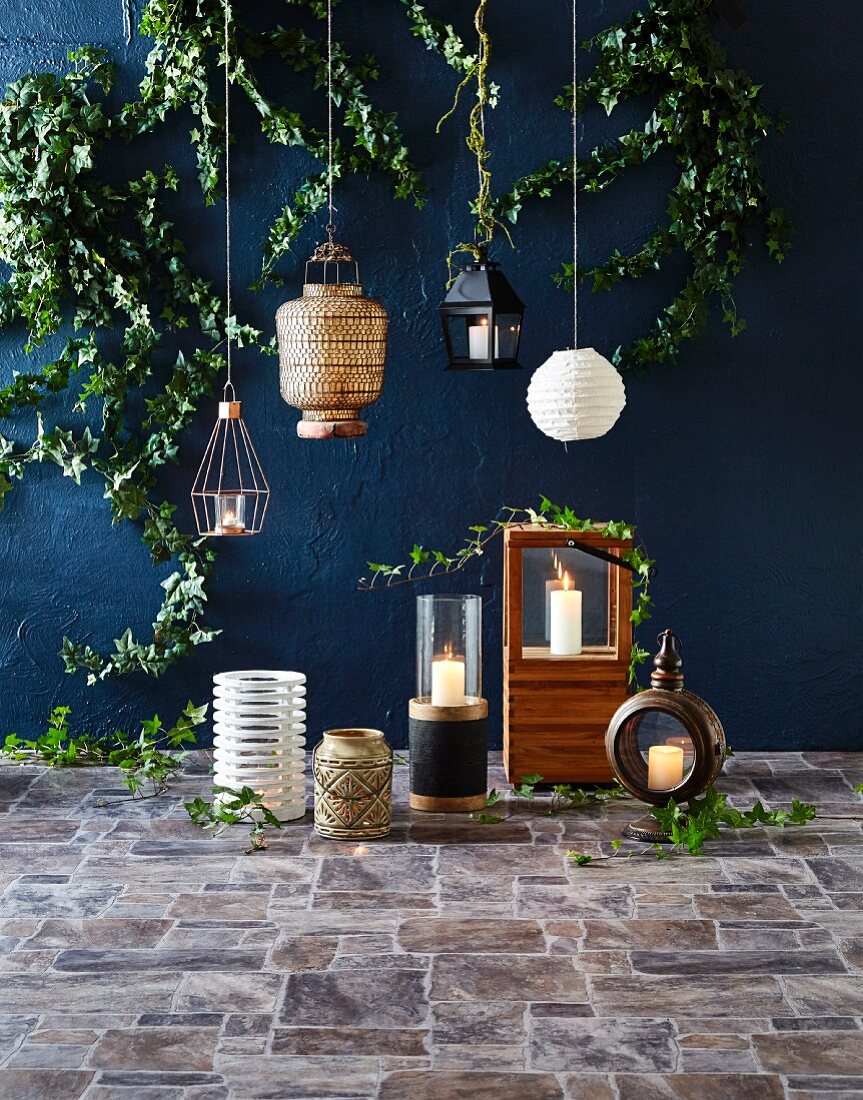 Hanging lamps in front of a wall painted dark blue, various lanterns with burning candles on tiled floors