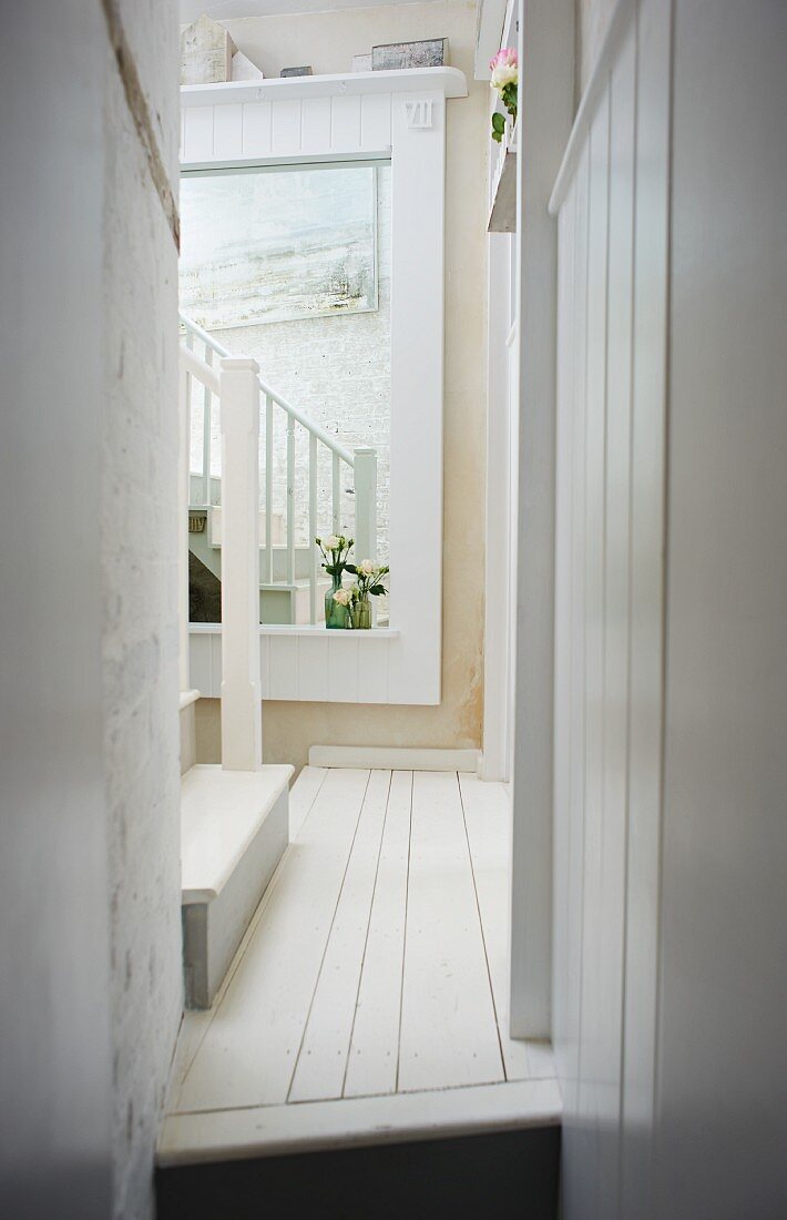 Schmaler Gang in ländlichem Haus mit weißem Dielenboden, an Wand im Hintergrund gerahmter Spiegel