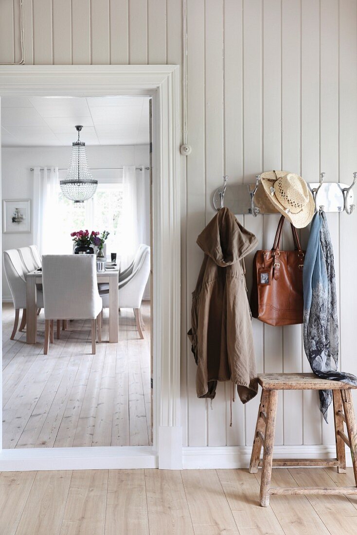 Rustic hallway with wall-mounted coat rack and dining area in background