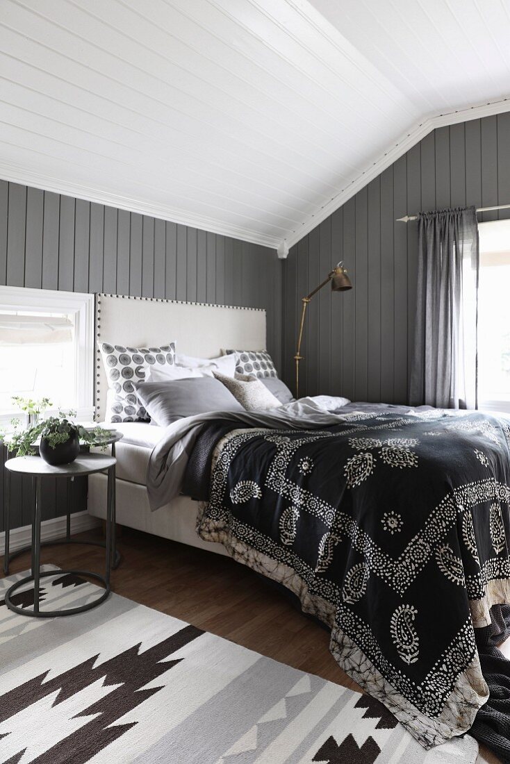 Schlafzimmer mit Ethno-Tagesdecke auf Doppelbett vor dunkelgrau gestrichener Holzwand