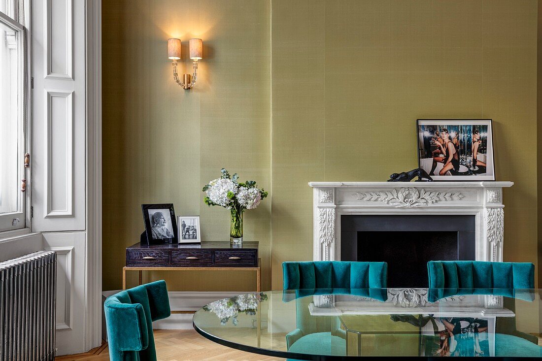 Glass table and green-painted wall in grand interior with fireplace