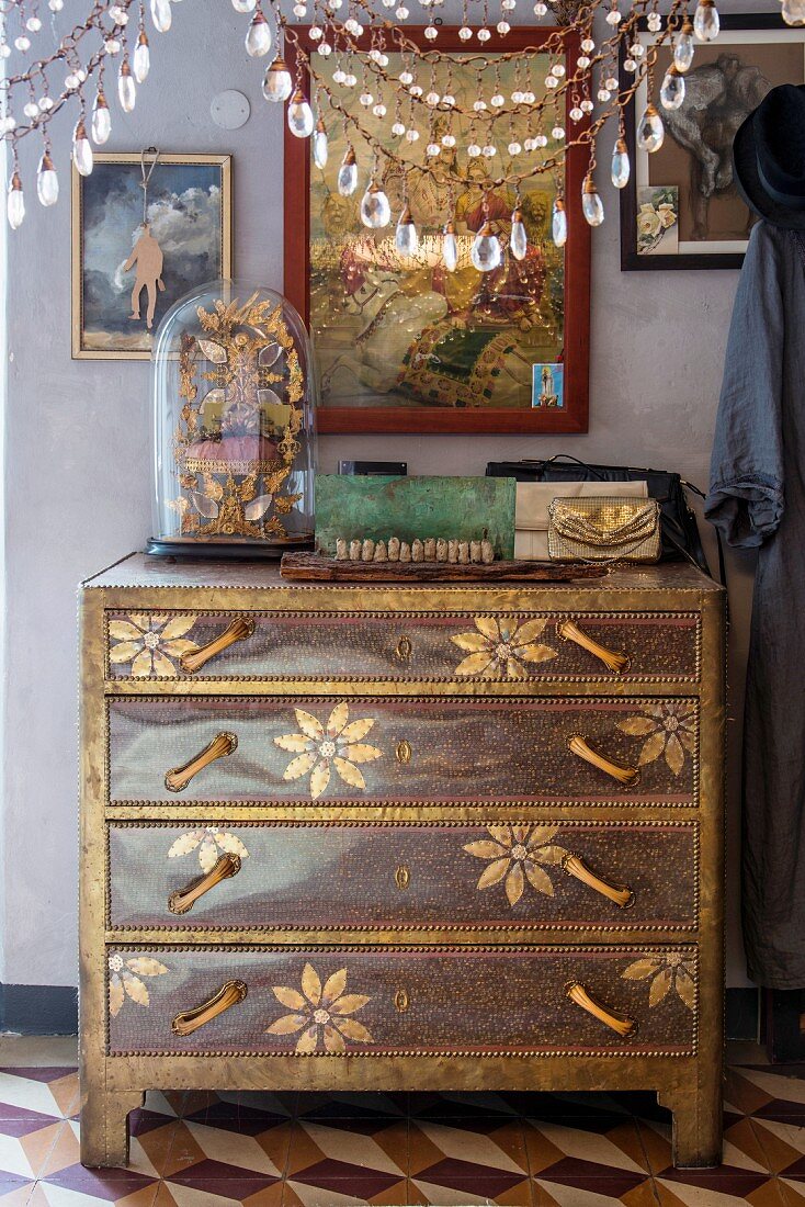 Antique finds on top of marquetry chest of drawers; glass pendants hanging from lampshade in foreground