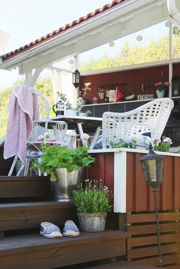 Sommerliche Veranda, rotbraun gestrichen mit Sitzplatz und weissen Rattanstühlen neben Holzstufen