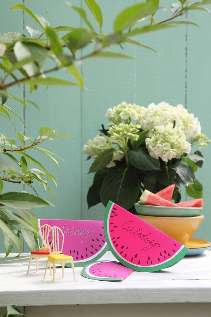DIY-Einladungskarte aus gefaltetem Papier in Melonenschnitzform auf Gartentisch