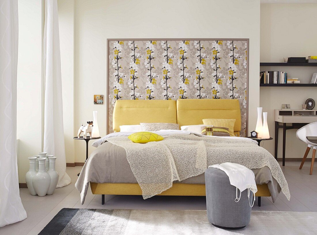 An elegant, feminine double bed with a light plaid and yellow cushions against a floral-papered frame at the head end