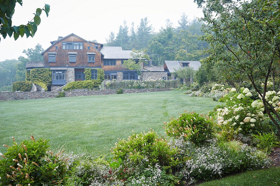 A spacious garden with a large lawn with an old arts-adn-crafts shingle house