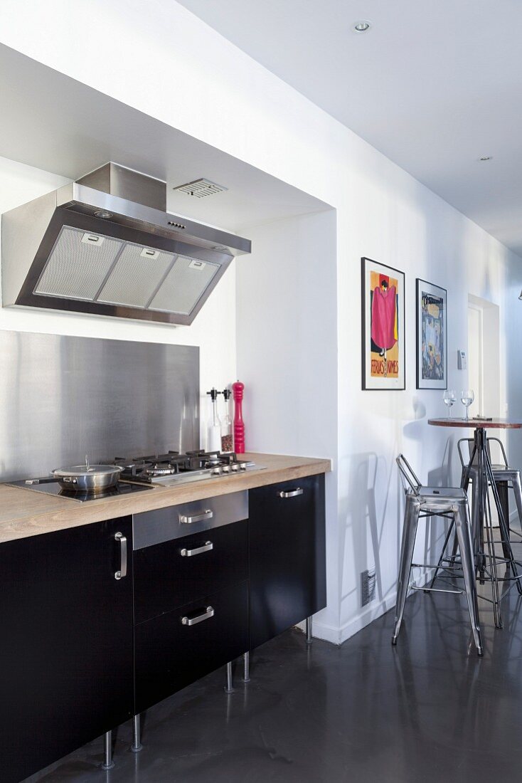 Küchenzeile mit Edelstahl-Spritzschutz und schwarzer Front in Wandnische