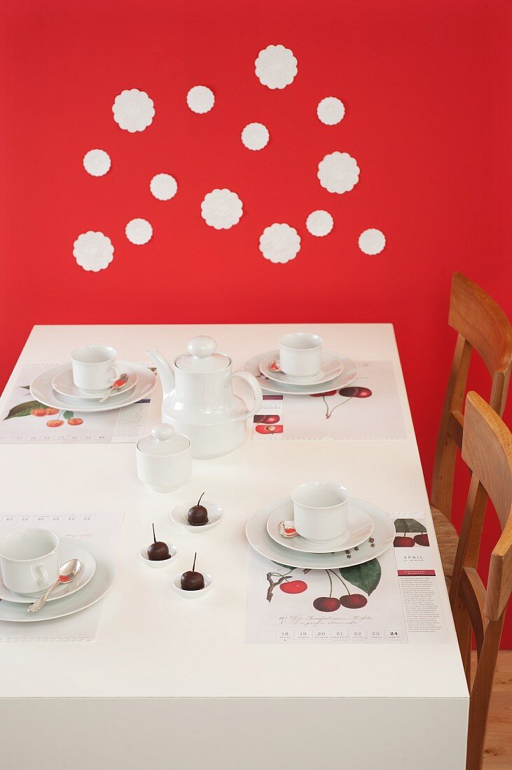 Gedeckter Kaffeetisch mit Kirschen vor roter Wand mit weissen Spitzenuntersetzer dekoriert