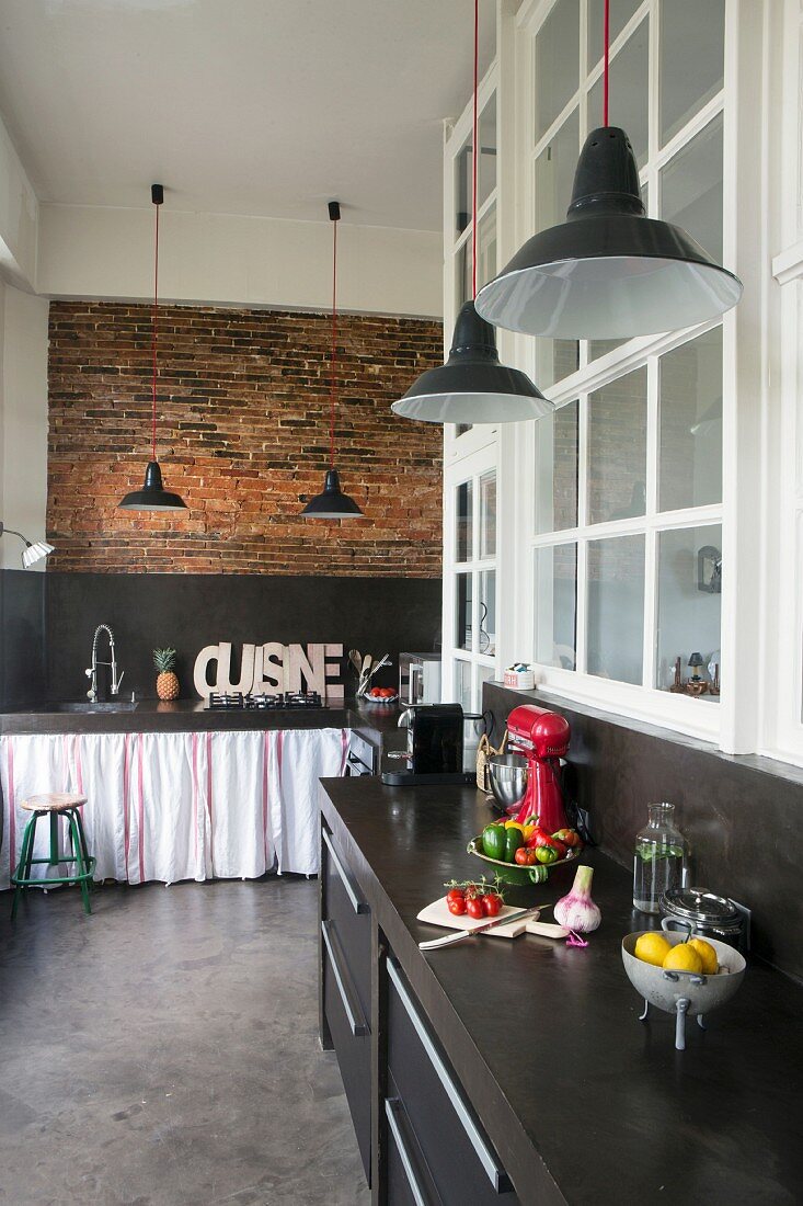 Schwarze Küchenzeilen in Loftwohnung mit Ziegelwand, Pendelleuchten und anthrazitfarbenem Betonboden