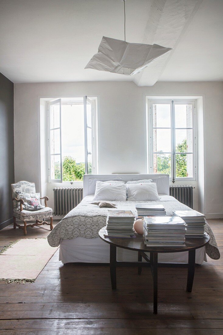 Schlafzimmer mit rustikalem Dielenboden, Doppelbett und rundem Holztisch mit Zeitschriftenstapeln