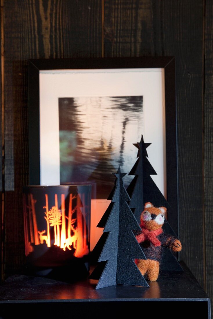 Atmospheric candle lantern and black Christmas-tree ornament on dark surface