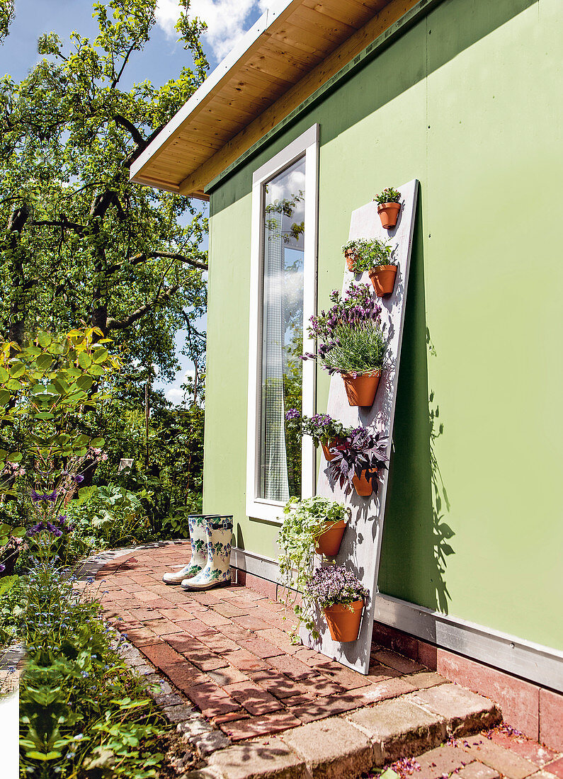 Wandpaneel mit Blumentöpfen an grüner Hauswand im Garten
