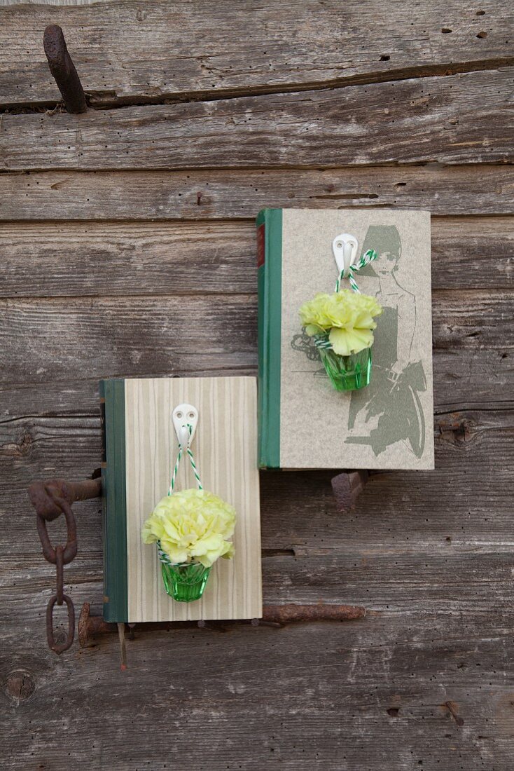 Buch als Vasenhalter: Grüne Nelken in Väschen an Garderobenhaken, am Buch befestigt
