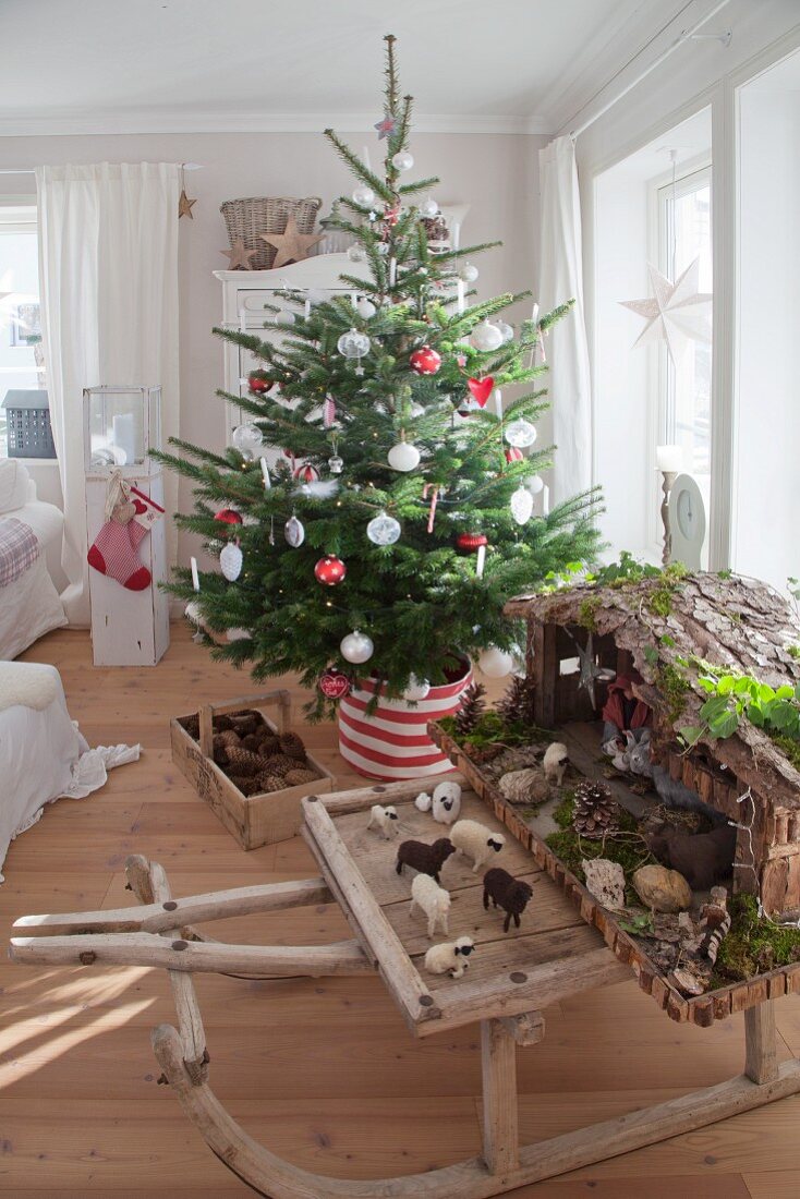 Geschmückter Weihnachtsbaum mit traditioneller Weihnachtskrippe auf Vintage Holzschlitten