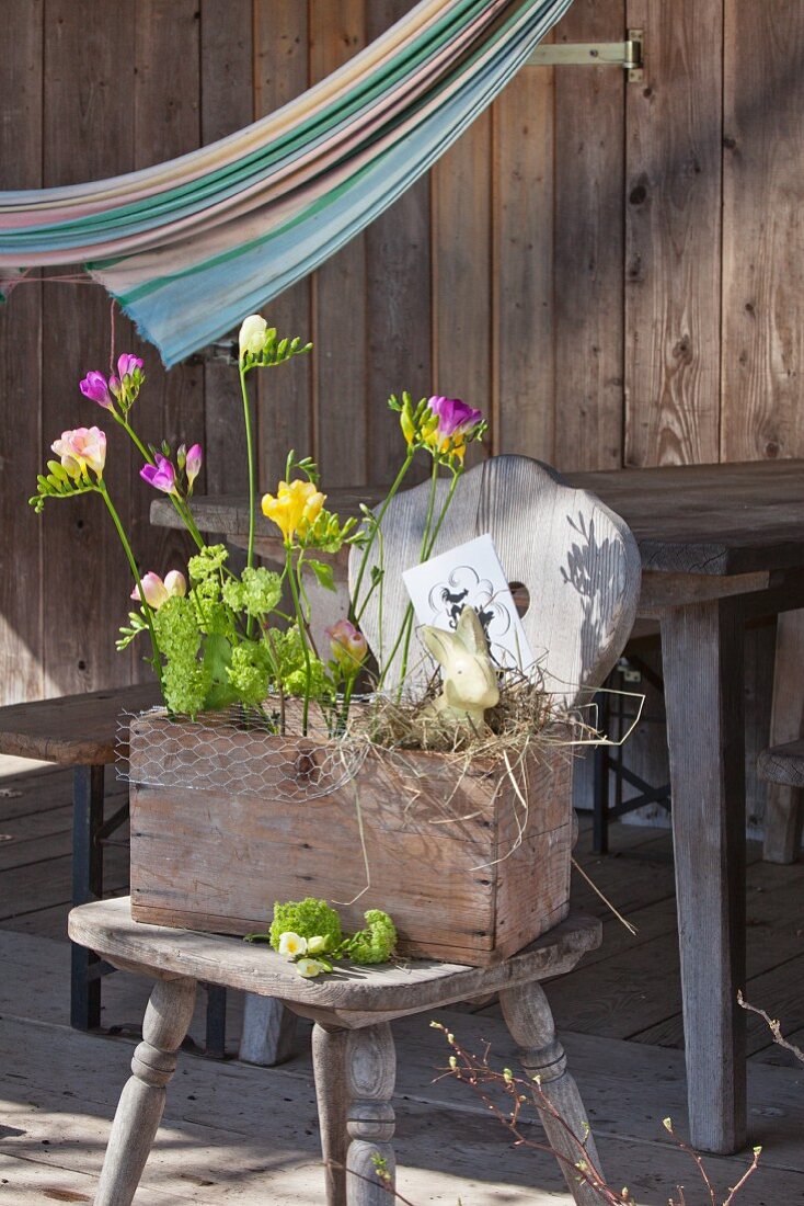 Blumen in einer rustikale Holzkiste mit Hasendraht auf Bauernstuhl