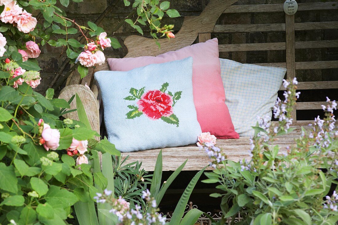 Romantischer, gestrickter Kissenbezug mit Rosenmotiv auf rustikaler Gartenbank