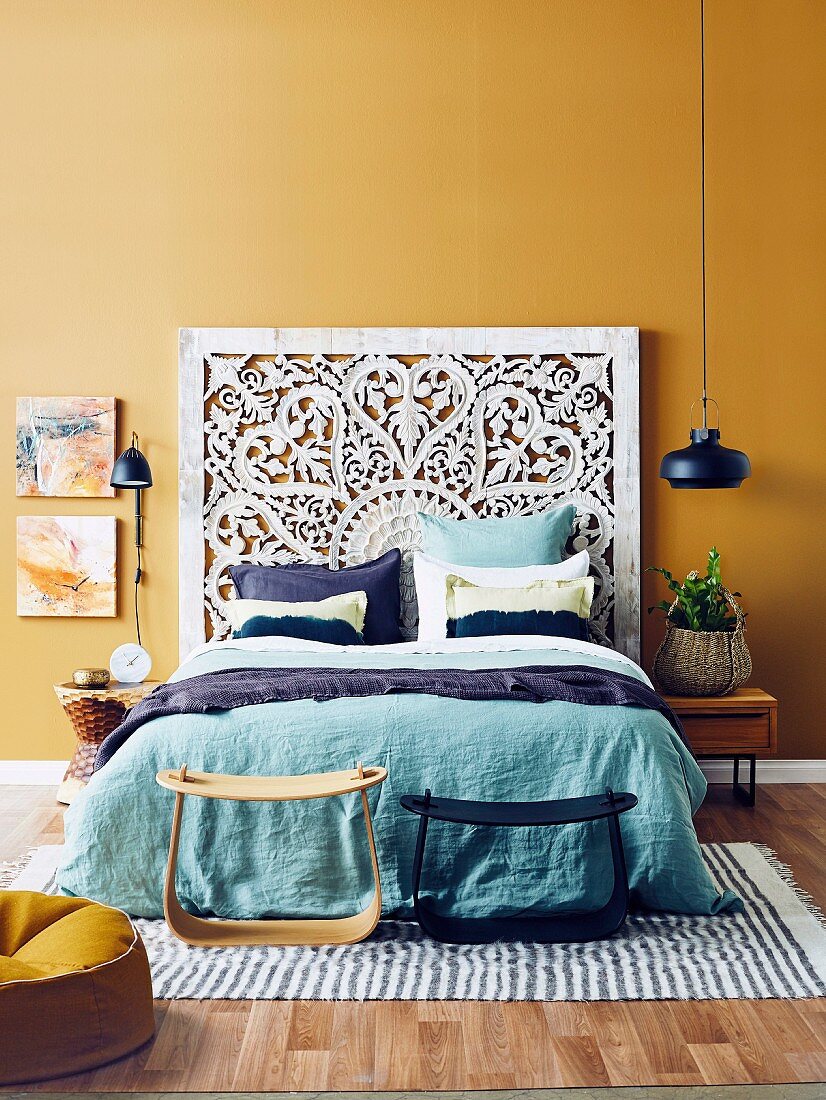 Doppelbett mit kunstvollem Betthaupt und türkisfarbene Bettwäsche vor ockerfarbener Wand